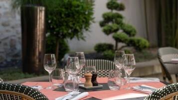 A dining table set with chairs, a stone wall, and a small tree in the background.