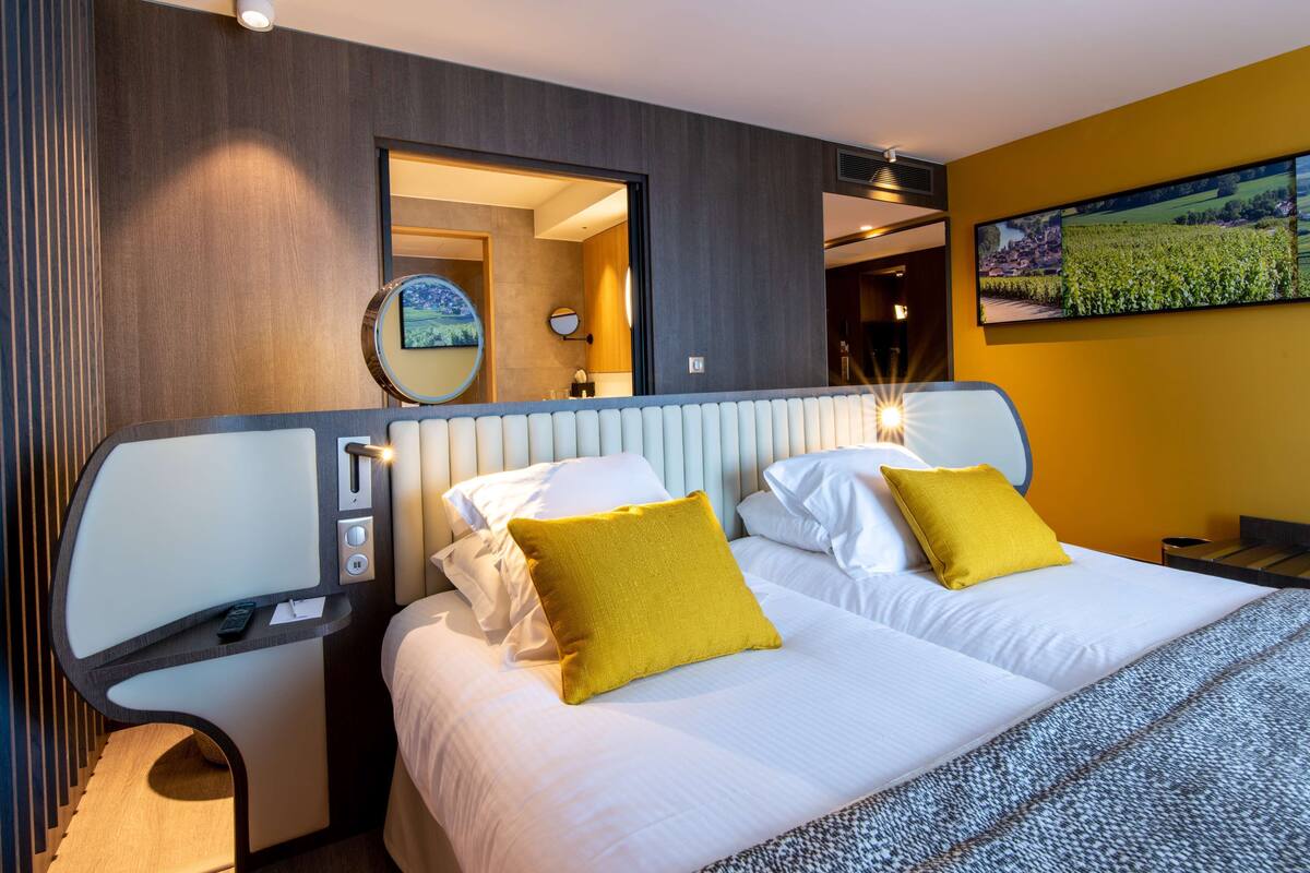 Moderni hotellihuone, jossa on suuri sänky, yöpöytä, peili ja seinälle asennettu televisio.