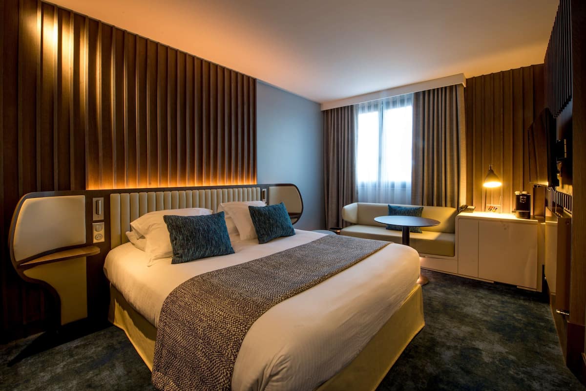 Hotellihuone, jossa on suuri sänky, sohva, pieni pöytä ja televisio.