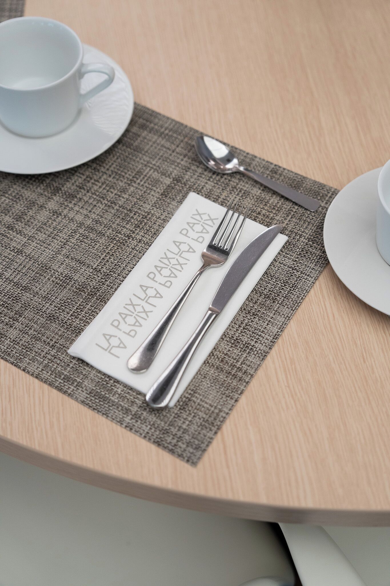 A neatly set dining table with a placemat, cutlery, and a cup.