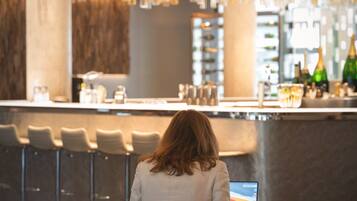 A person seated at a table with a laptop, a bar area with stools, and a modern interior design with hanging lights.