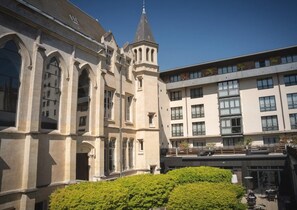 A historic building with arched windows and a tower, adjacent to a modern building with balconies and large windows.