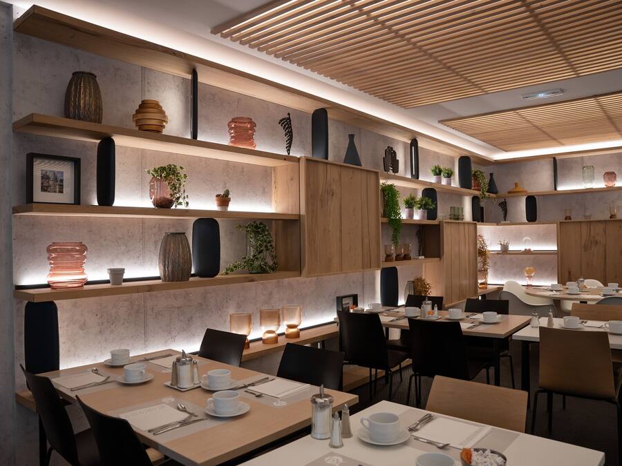 Un espace repas moderne avec des tables et des chaises en bois, des étagères ornées d’objets décoratifs et un plafond avec des lambris en bois.