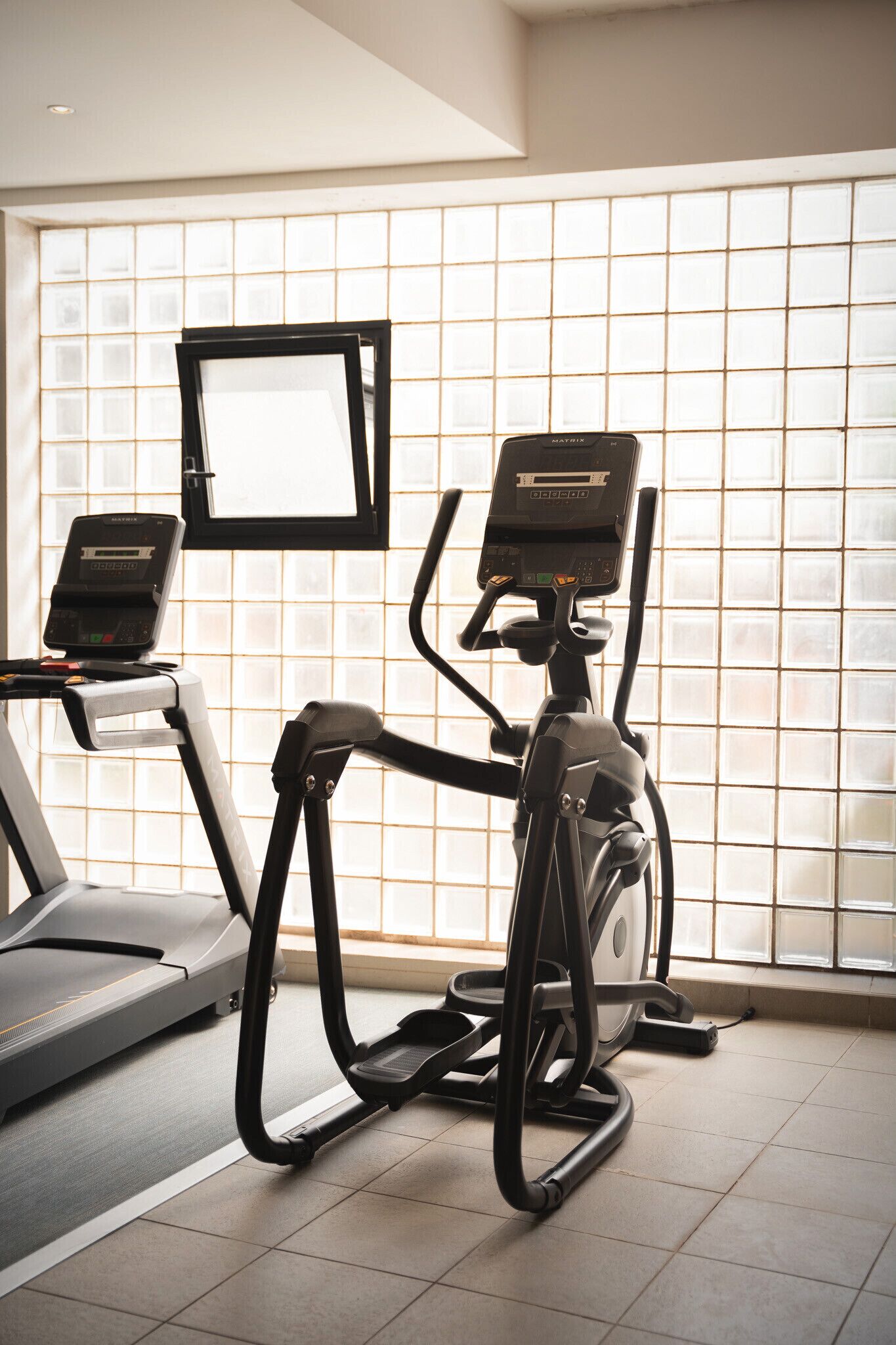 A gym with treadmills and an elliptical machine, a TV screen, and a window with a view.