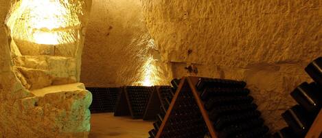 An underground wine cellar with stone walls and wooden racks holding wine bottles.