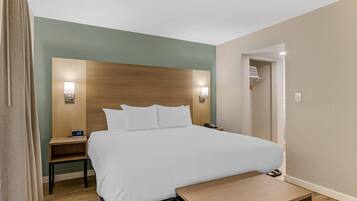 A hotel room with a large bed, bedside tables, a nightstand, a desk, and a chair.