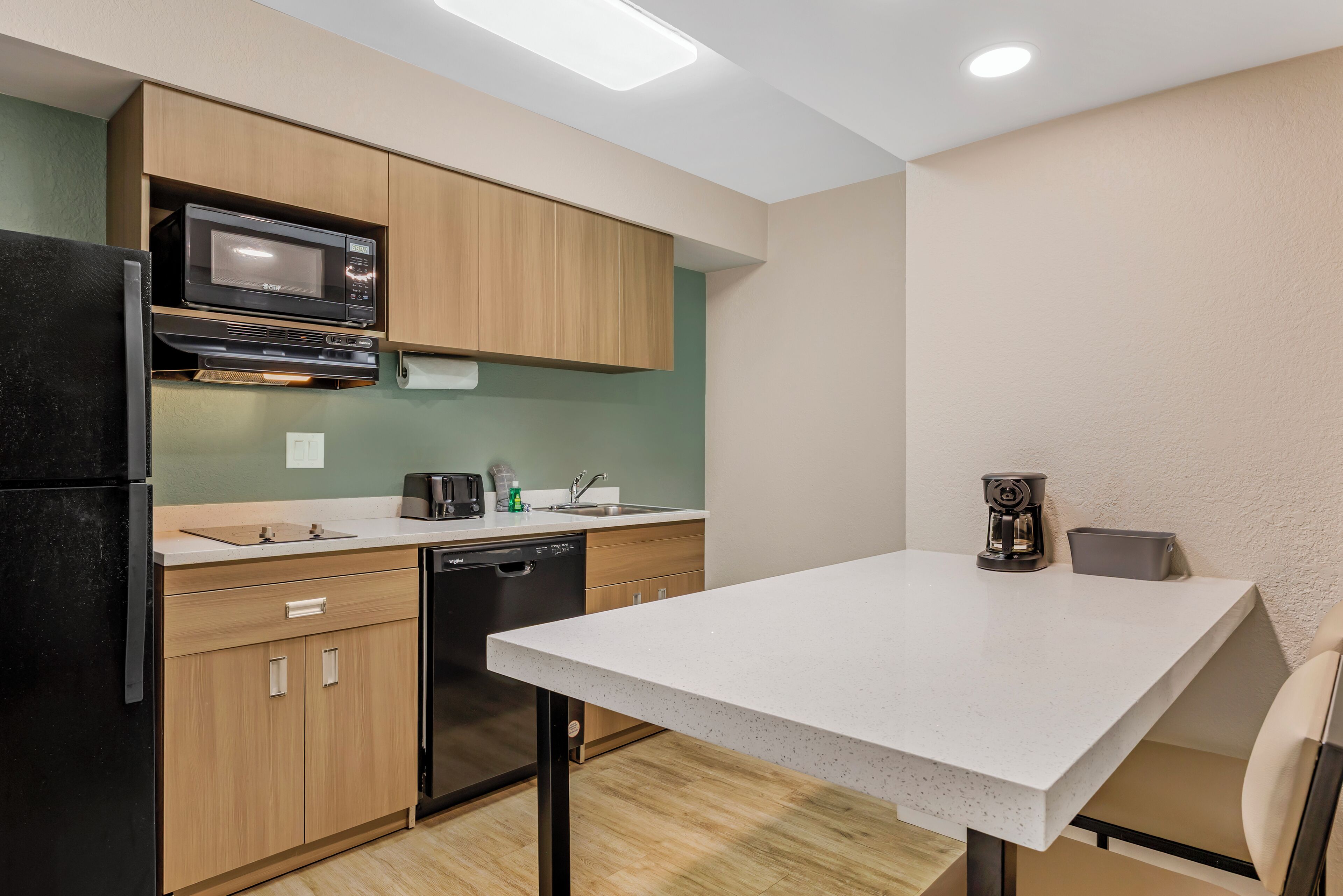 A compact kitchen with wooden cabinets, a microwave, a dishwasher, and a coffee maker.
