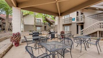 An outdoor patio with tables and chairs, a barbecue grill, and a staircase leading to a balcony.