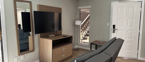 A modern living room with a flat-screen TV, wooden entertainment unit, a bench, and a door.