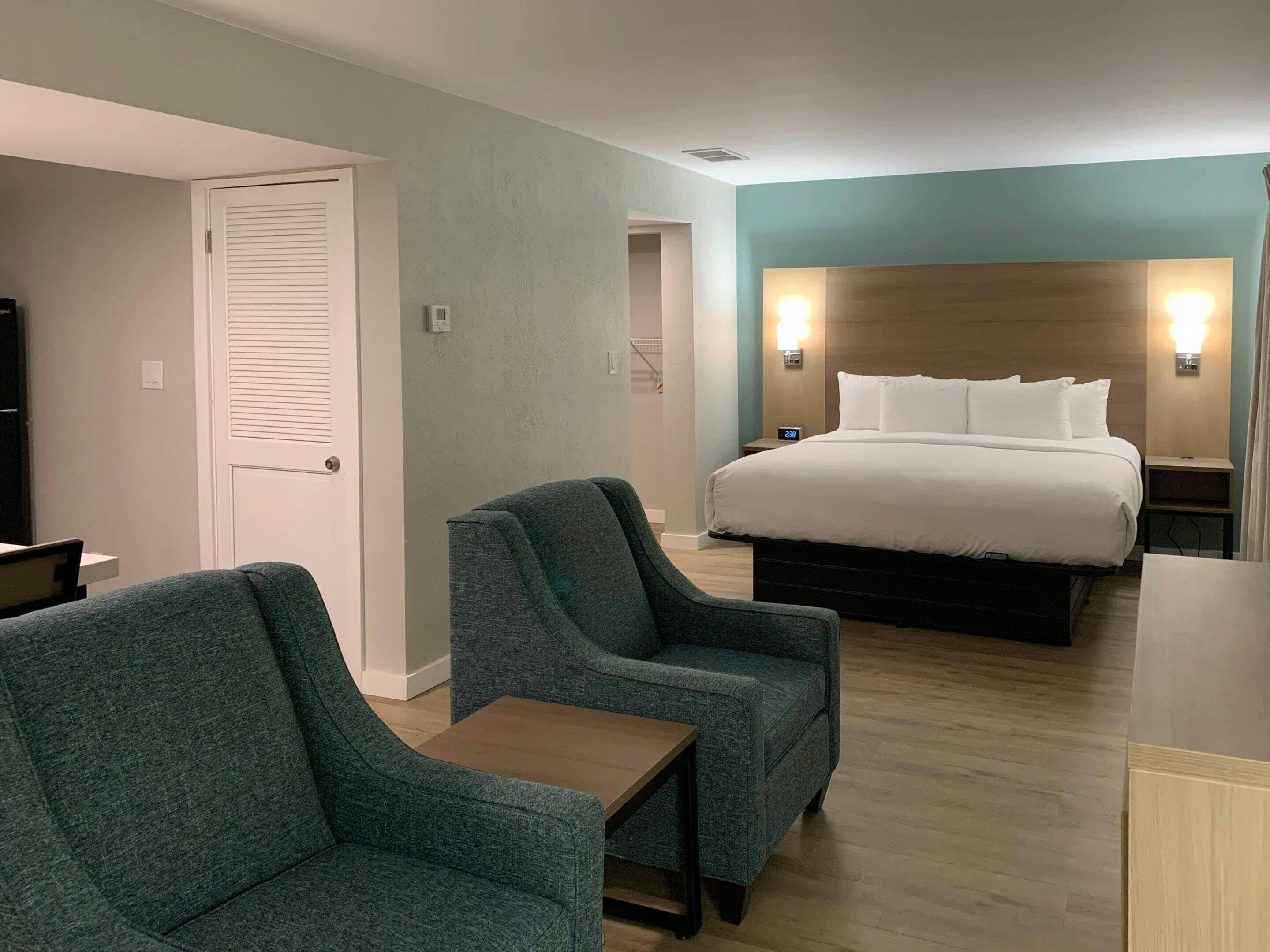 A hotel room with a bed, two armchairs, a small table, and a nightstand with a lamp.
