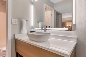 A modern bathroom with a white sink, a large mirror, and a wooden vanity.