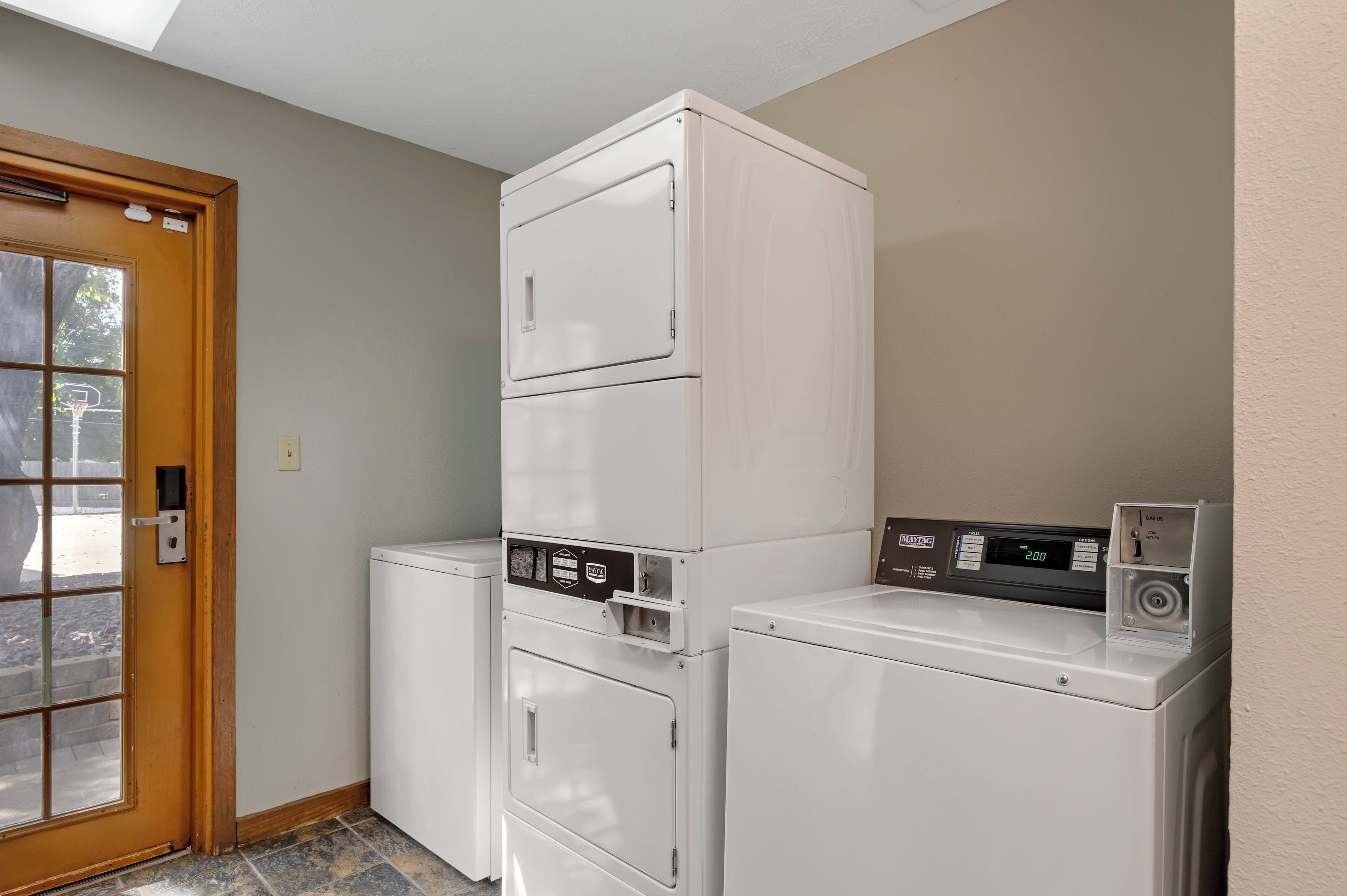 A laundry room with three stacked washers and dryers, a wooden door, and a window.