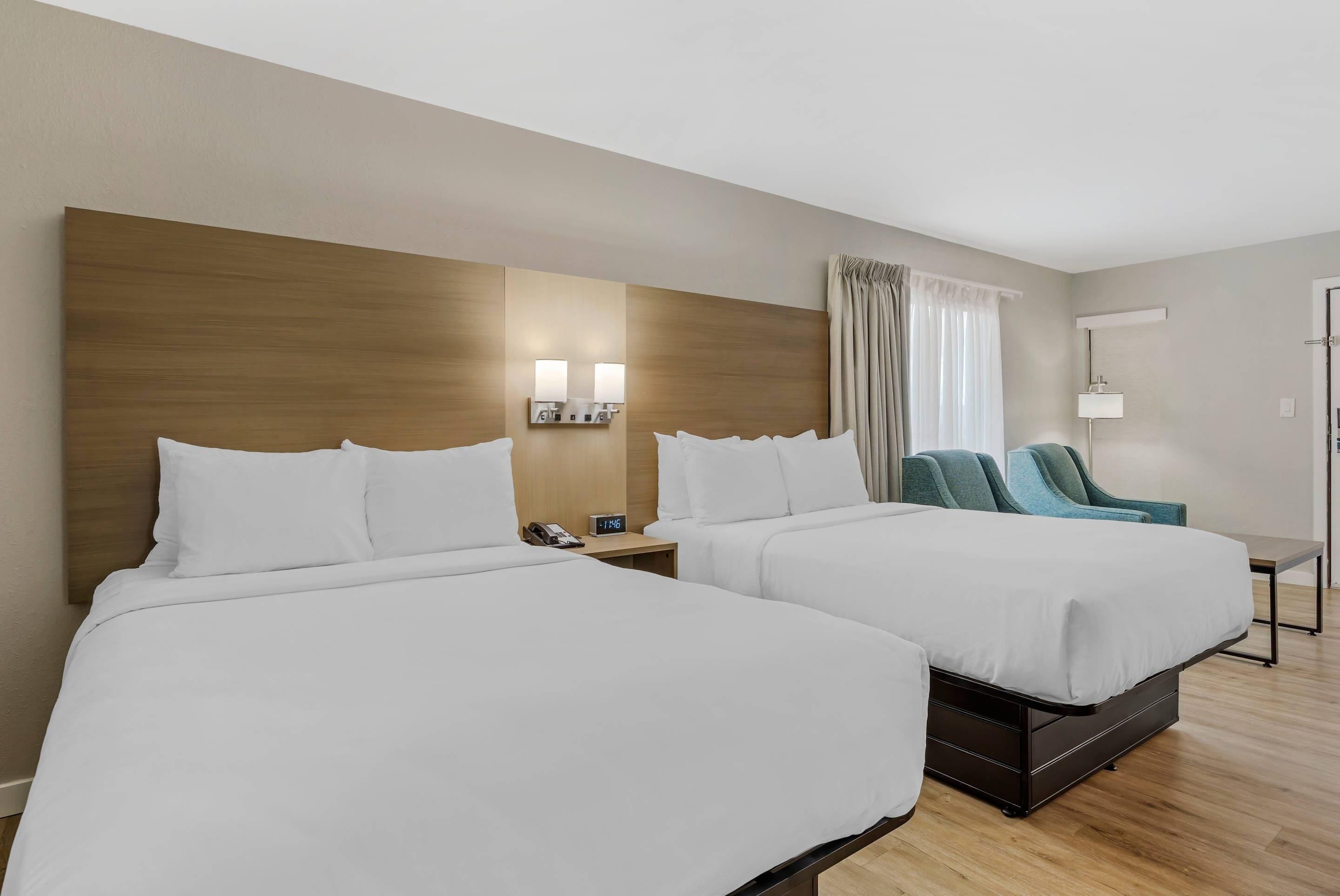 A hotel room with two beds, a nightstand with a phone, a lamp, and a chair.