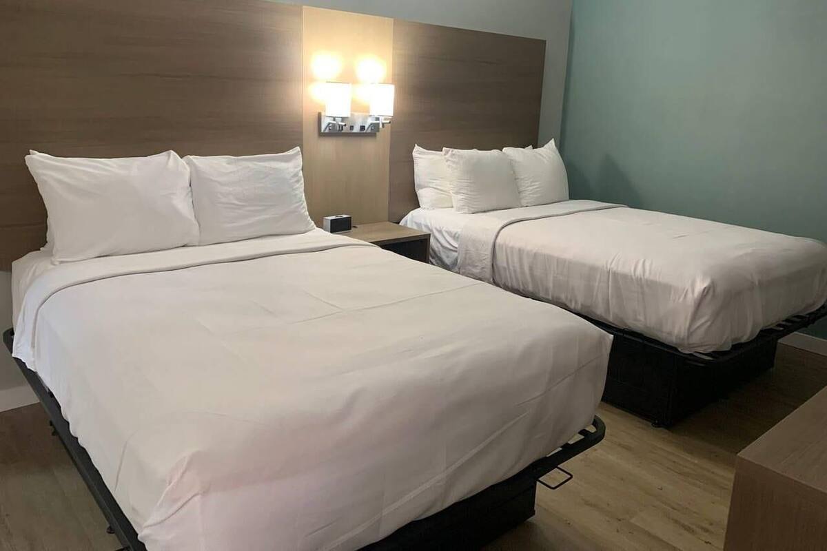 Hotellihuone, jossa on kaksi sänkyä, puinen pääty ja seinään asennetut valaisimet.