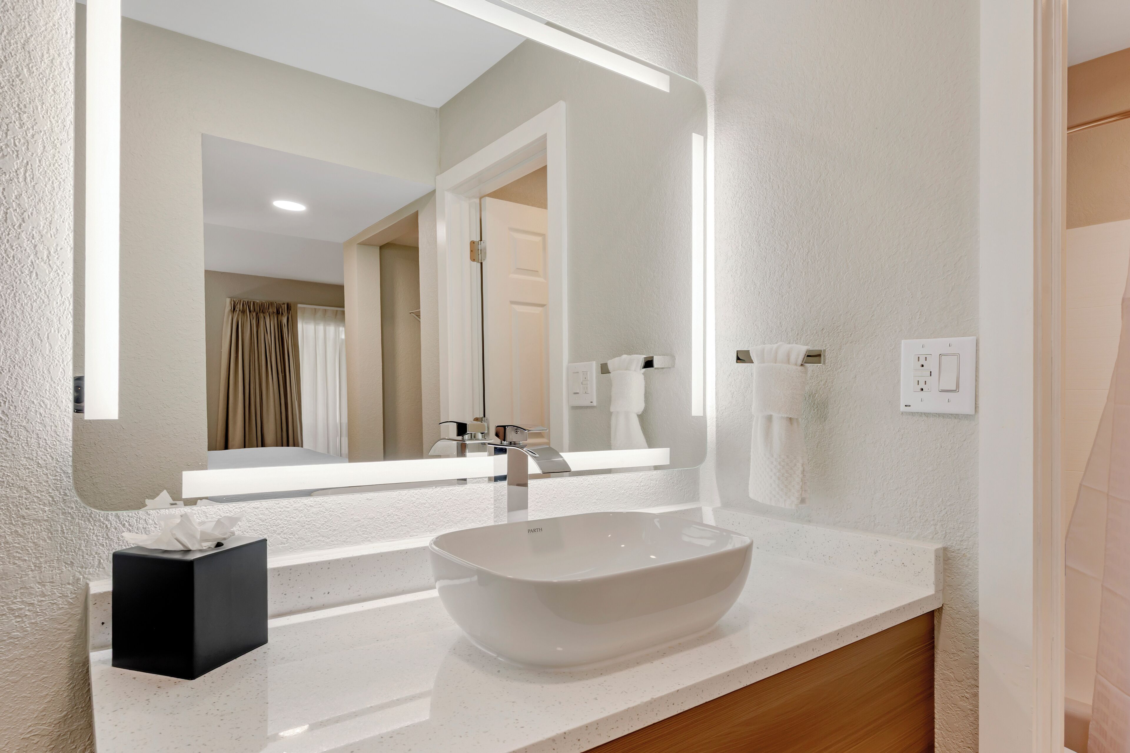 Une salle de bain moderne avec un lavabo blanc, un grand miroir et un distributeur de serviettes.