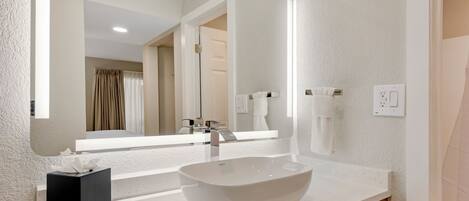 A modern bathroom with a white sink, a large mirror, and a towel dispenser.