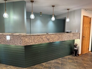 Reception area with a granite countertop and dark paneling, featuring a wooden door and a decorative statue.