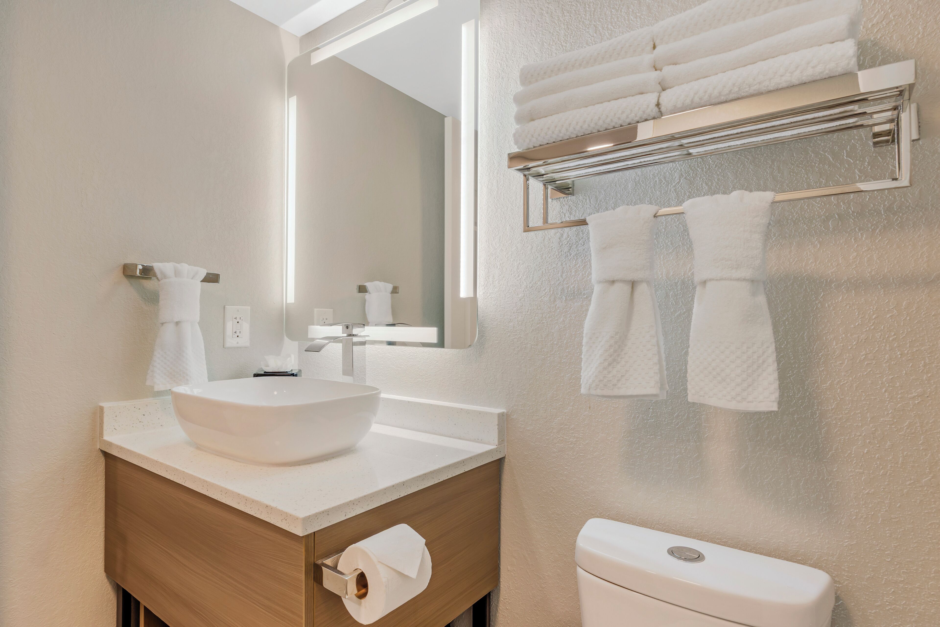 A modern bathroom with a large white sink, a mirror, and a towel rack with multiple towels.