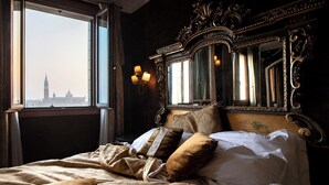 A bed with a view of a tower through a window, ornate headboard, and wall sconces. - Hotel Metropole Venezia (Venice)