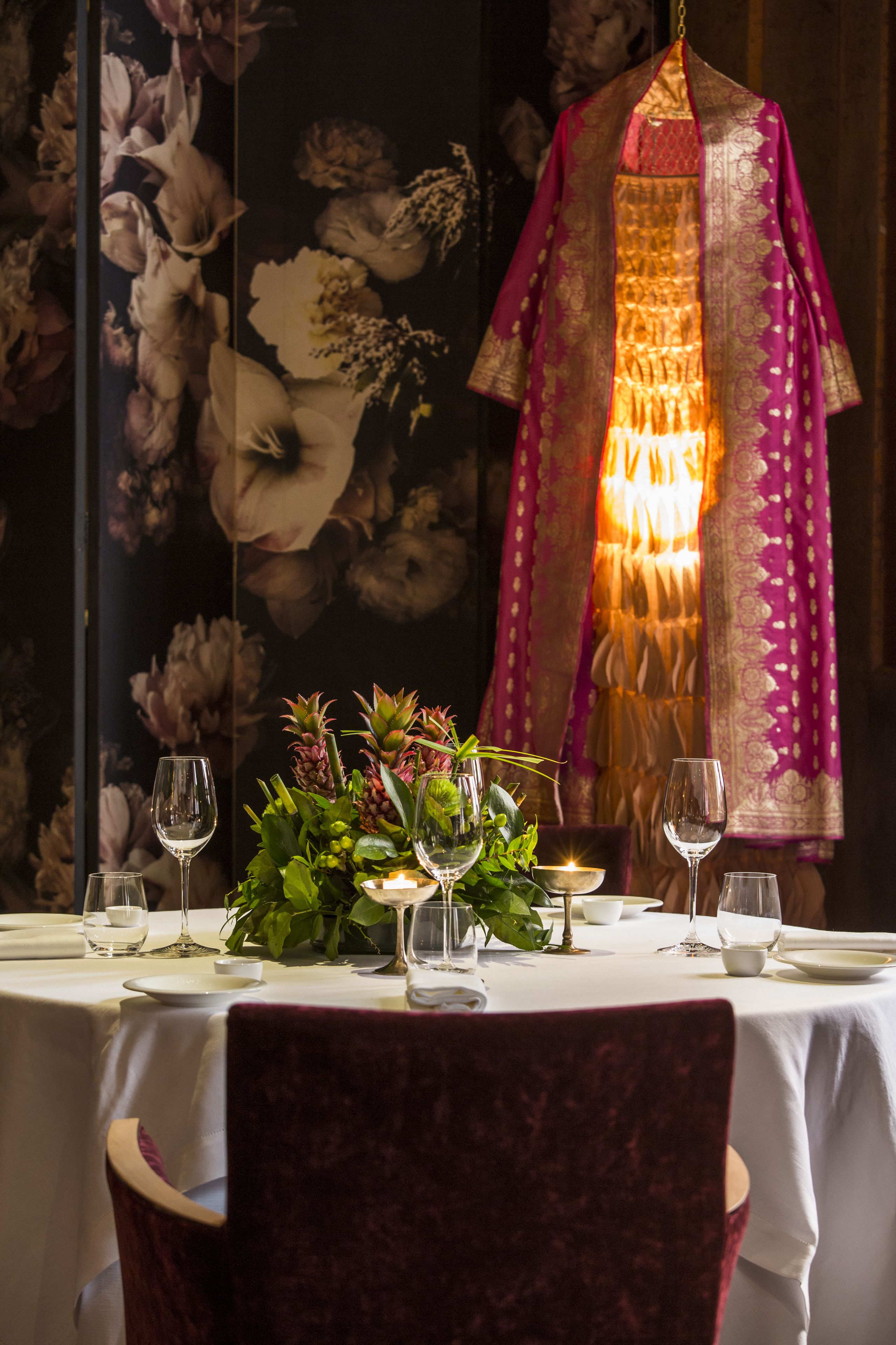 A dining table set with white tablecloths, candles, and a floral centerpiece.