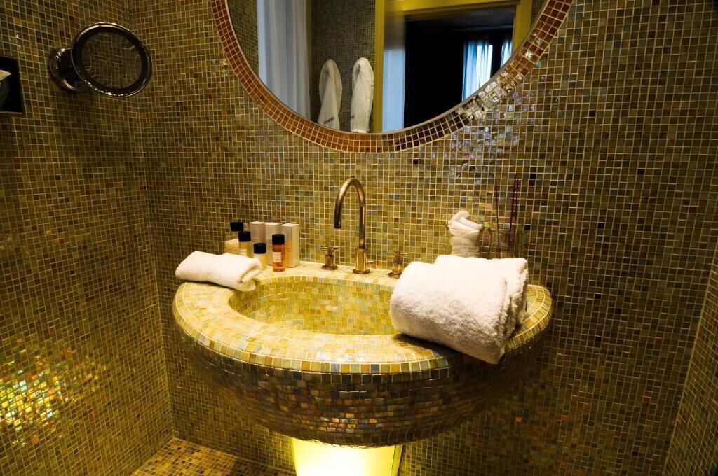 Uma casa de banho com lavatório em mosaico, um espelho redondo e um porta-toalhas.
