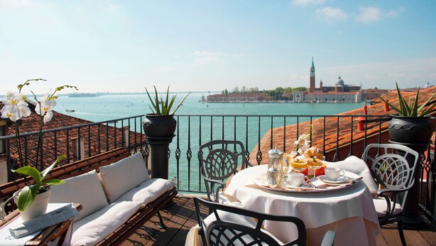 A terrace with a table set for breakfast overlooking a body of water and a historic building. - Hotel Metropole Venezia (Venice)