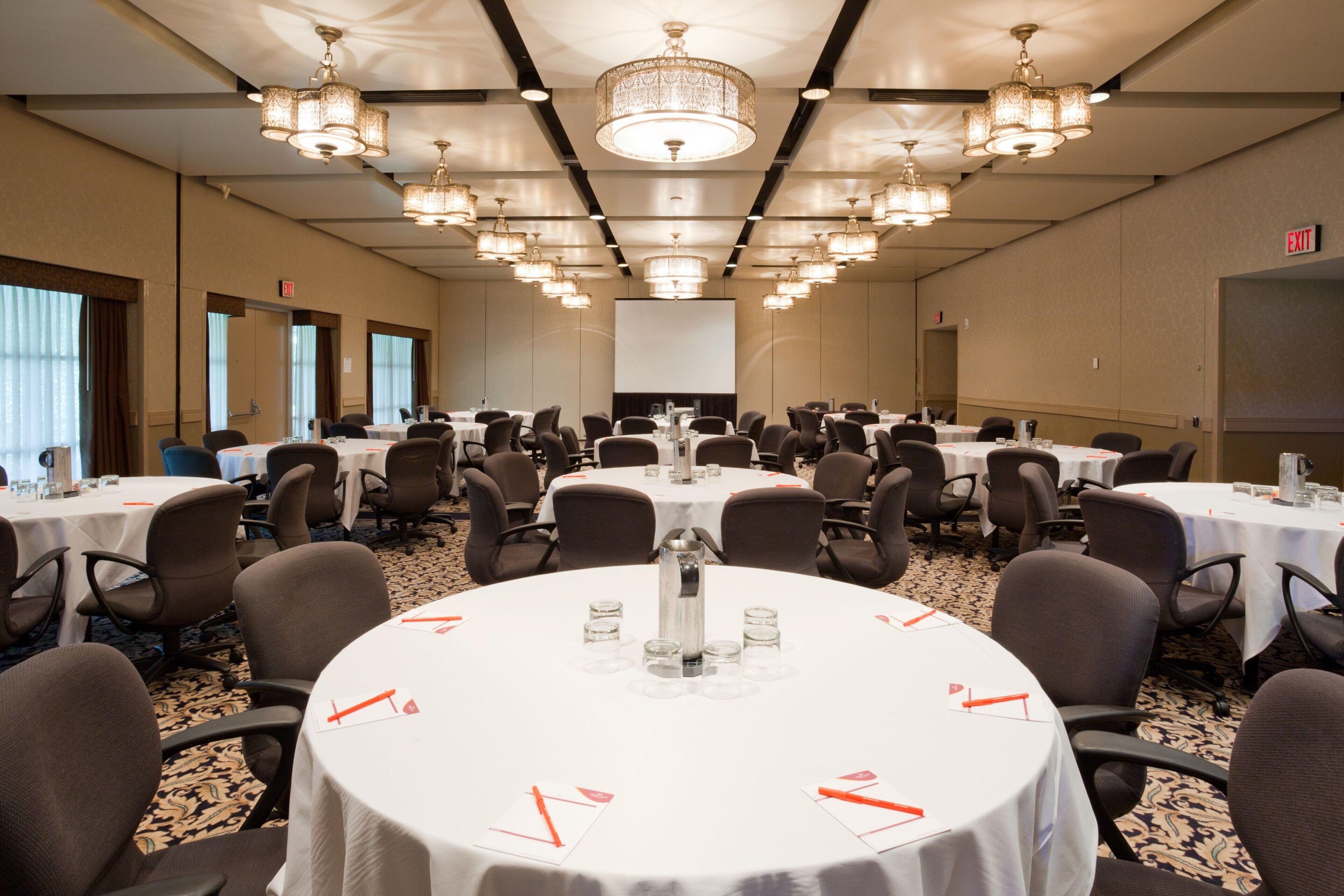 A conference room with round tables, chairs, and a large screen at the front.