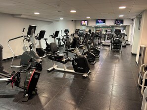 Un gimnasio con varias máquinas de cardio, incluyendo cintas de correr y bicicletas estáticas, dispuestas en filas.