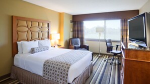 Habitación de hotel con una cama grande, un escritorio con televisor de pantalla plana, una silla y una ventana con cortinas.