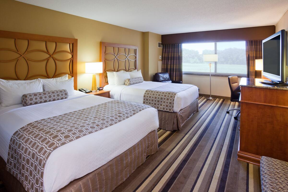 A hotel room with two beds, a desk, a chair, a television, and a window with a view of the outdoors.