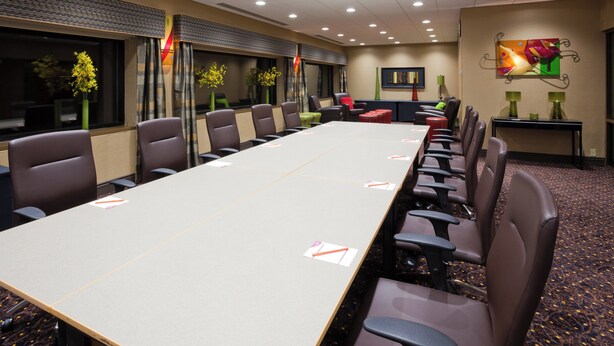 Ein Konferenzraum mit einem langen Tisch, mehreren Stühlen und Teppichboden.