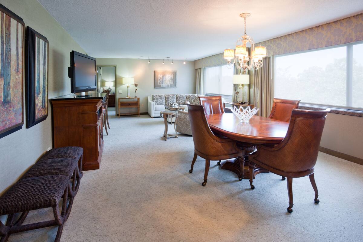 A hotel dining area with a wooden table, chairs, and a television on a stand.