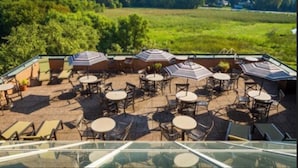Une terrasse extérieure dotée de plusieurs tables et chaises, entourée de verdure et offrant une vue dégagée sur le paysage.