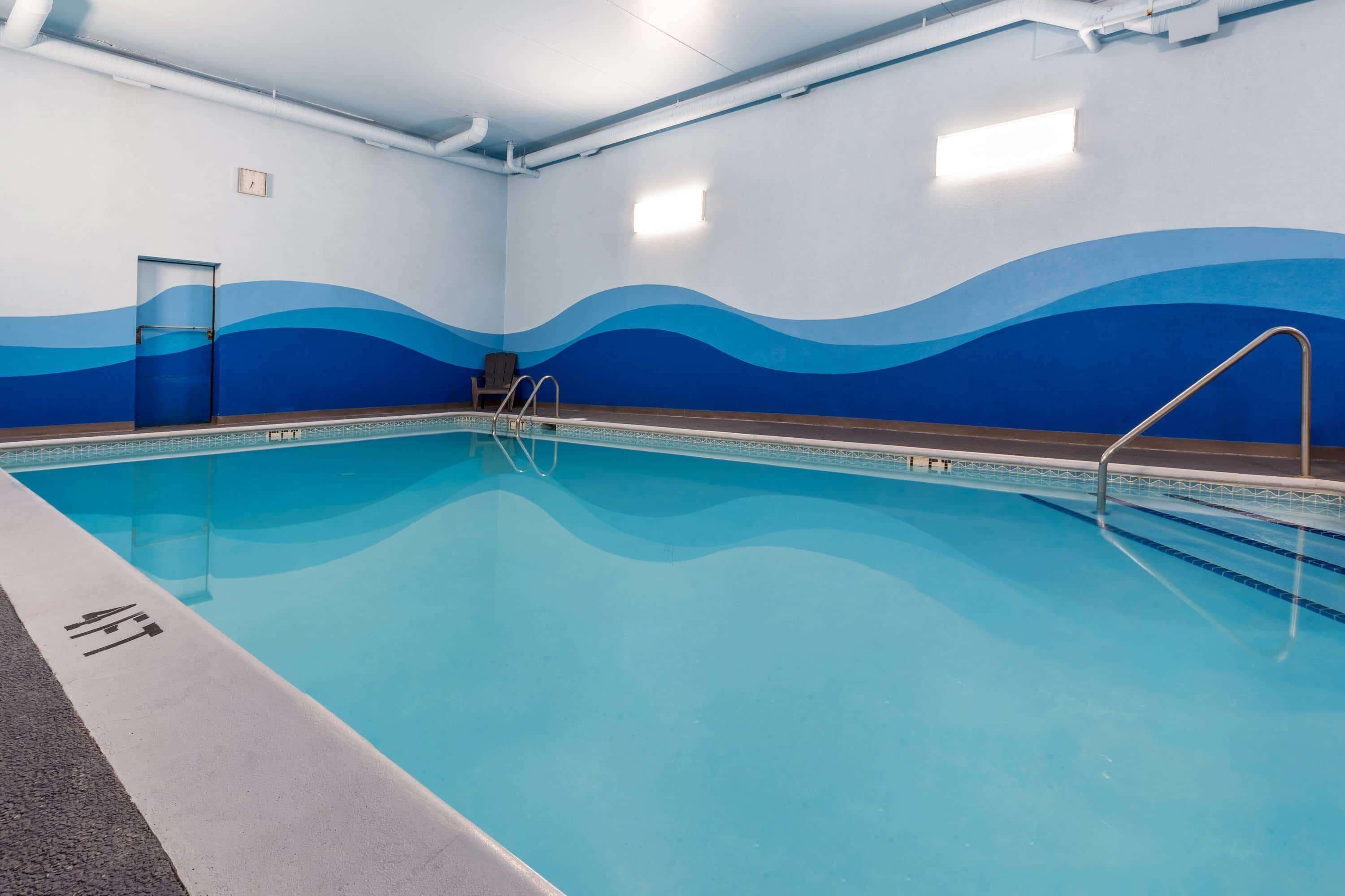 An indoor swimming pool with wave-patterned walls, a pool ladder, and a door.