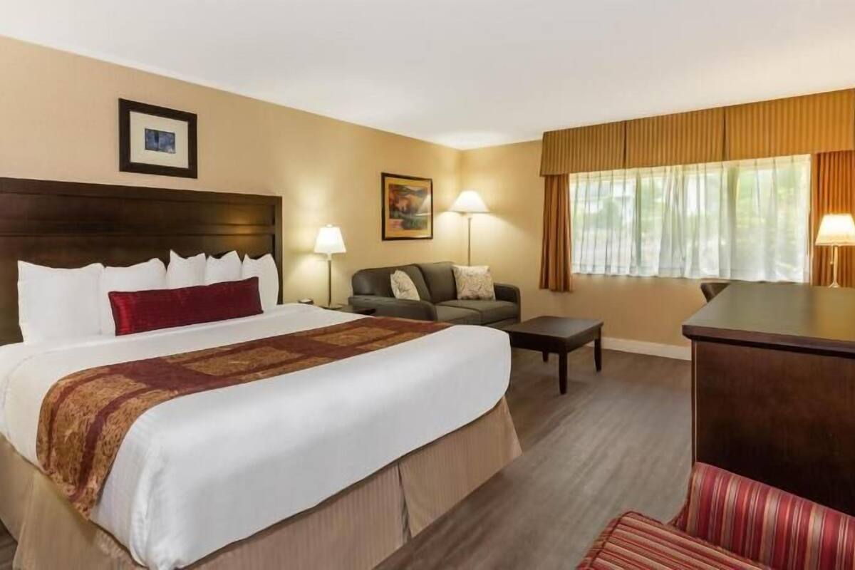 Ein Hotelzimmer mit einem großen Bett, einem Sofa, einem Schreibtisch und einem Fenster mit Vorhängen.