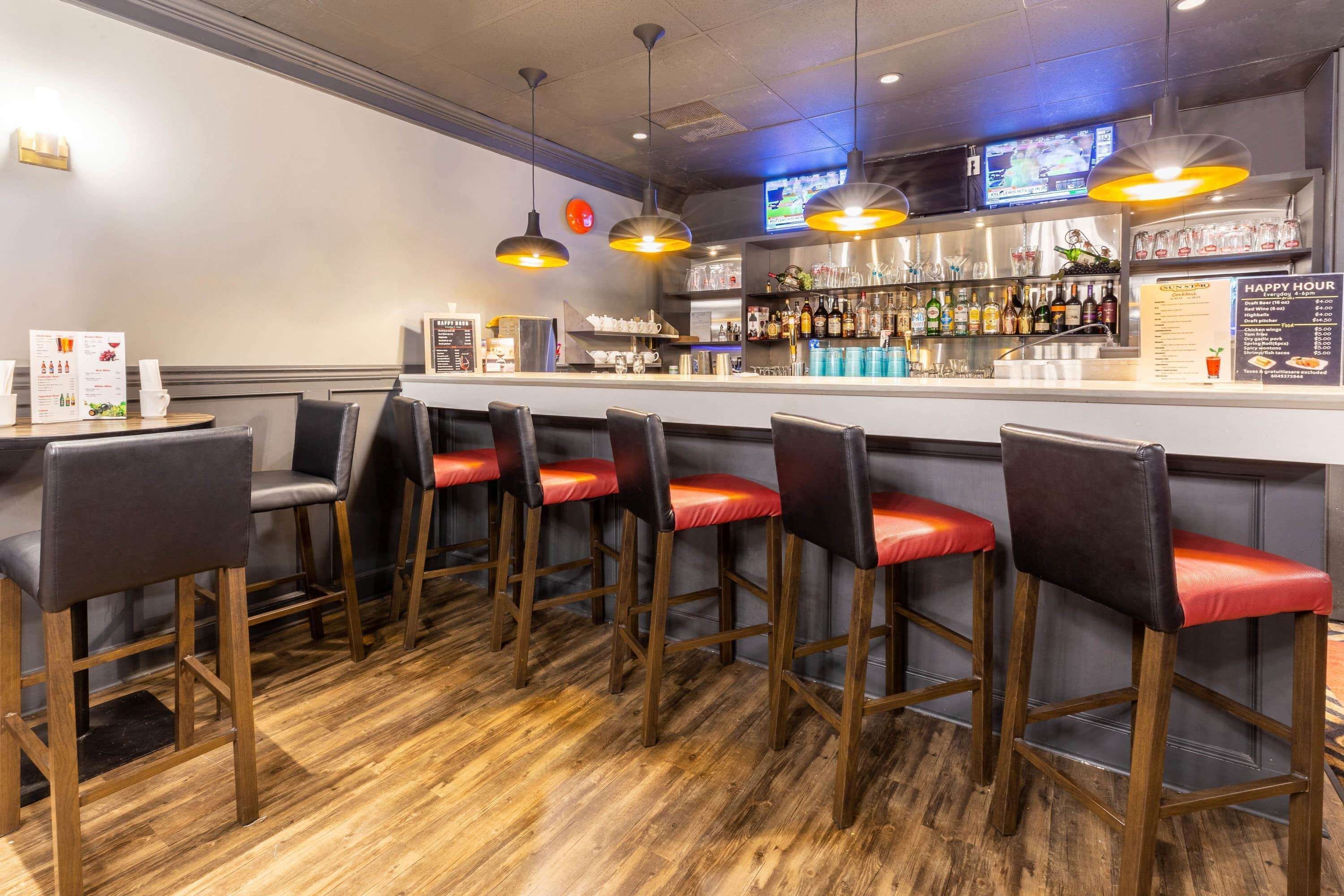 A bar area with wooden bar stools, a counter with a menu, and a television mounted above the bar.