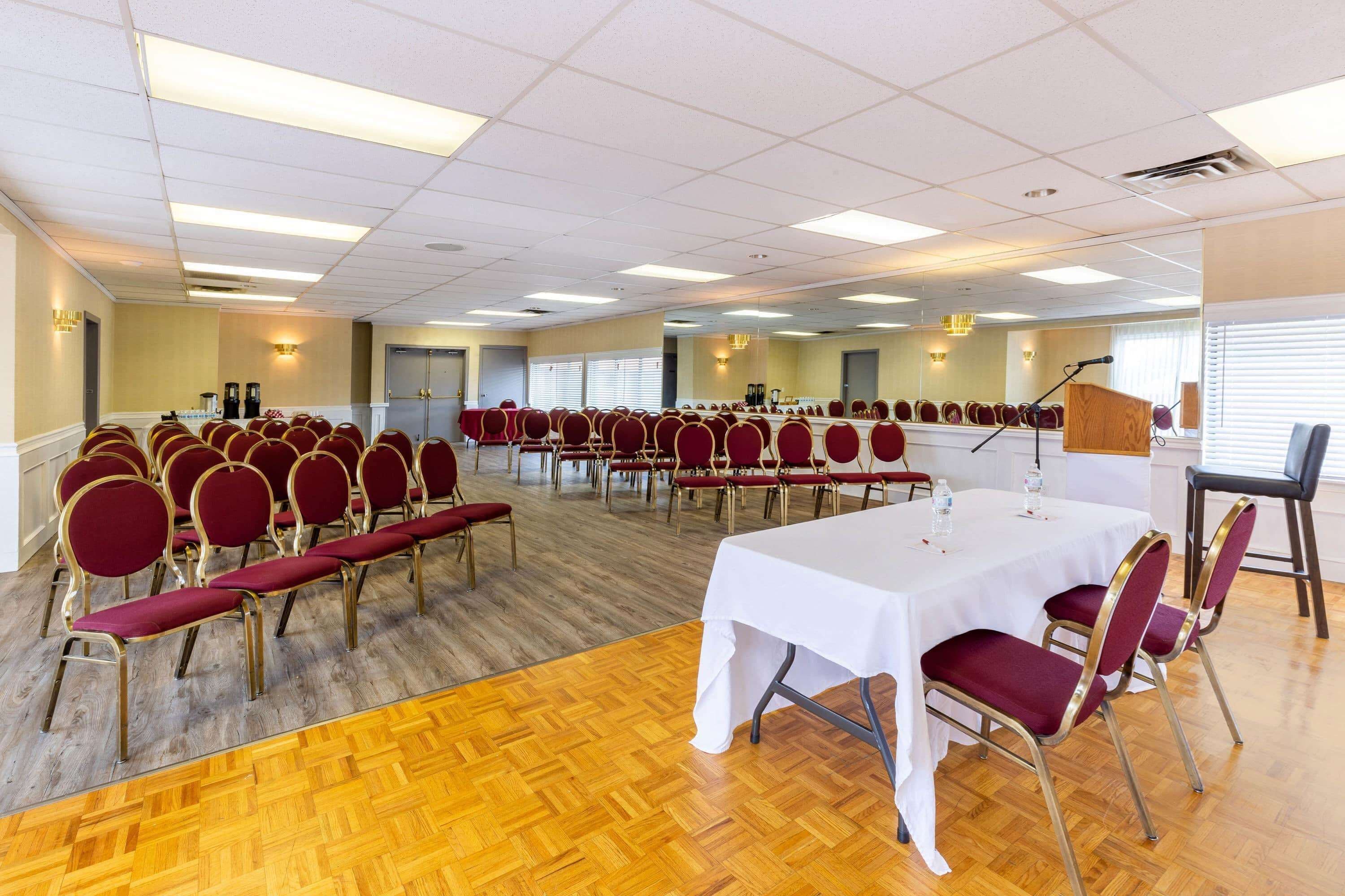 A conference room with rows of red chairs, a white table, and a wooden floor.