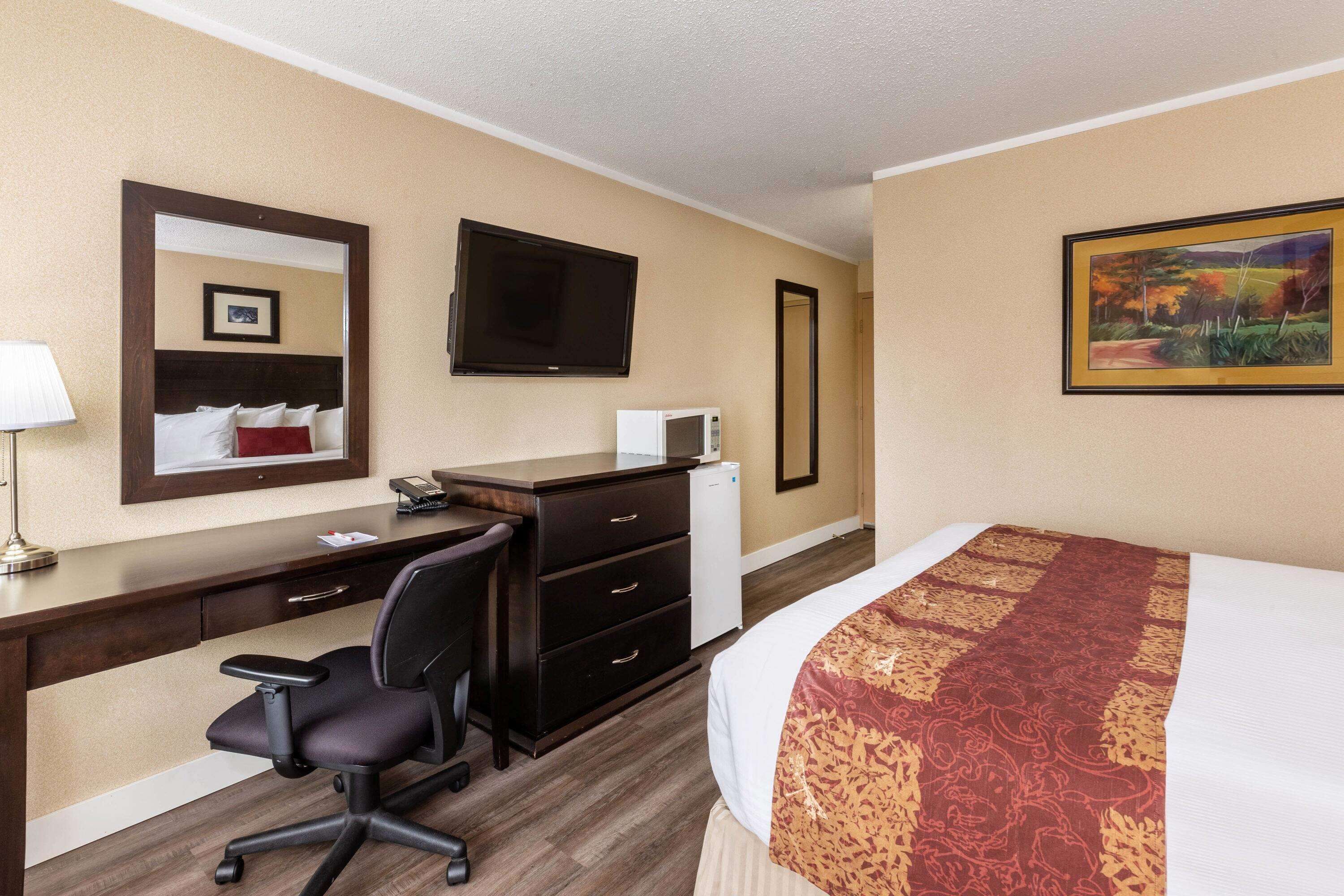 A hotel room with a bed, a desk with a chair, a television, a microwave, and a painting on the wall.