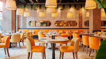 A restaurant with round tables, orange chairs, and hanging lamps.