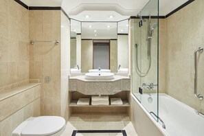 Un baño moderno con ducha de vidrio, bañera, inodoro y tocador con lavamanos y espejo.