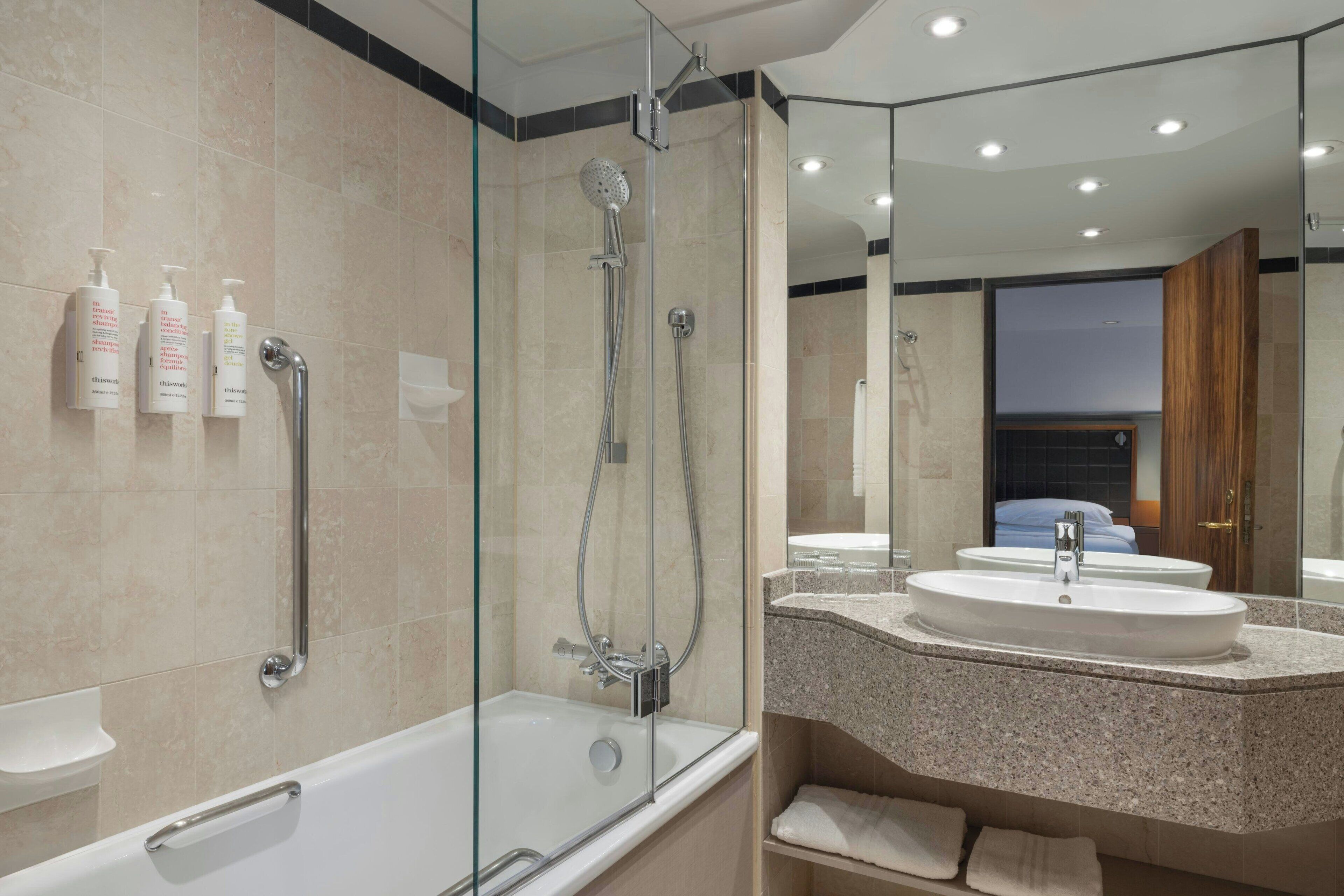 Un baño moderno con ducha de vidrio, una bañera blanca y un lavamanos con encimera de granito.