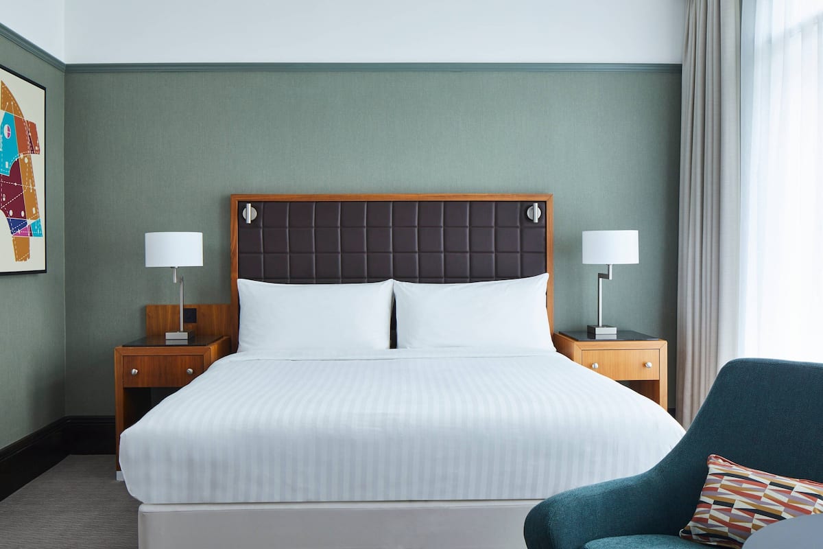 A neatly made bed with a dark headboard, two bedside tables with lamps, and a chair with a patterned cushion.