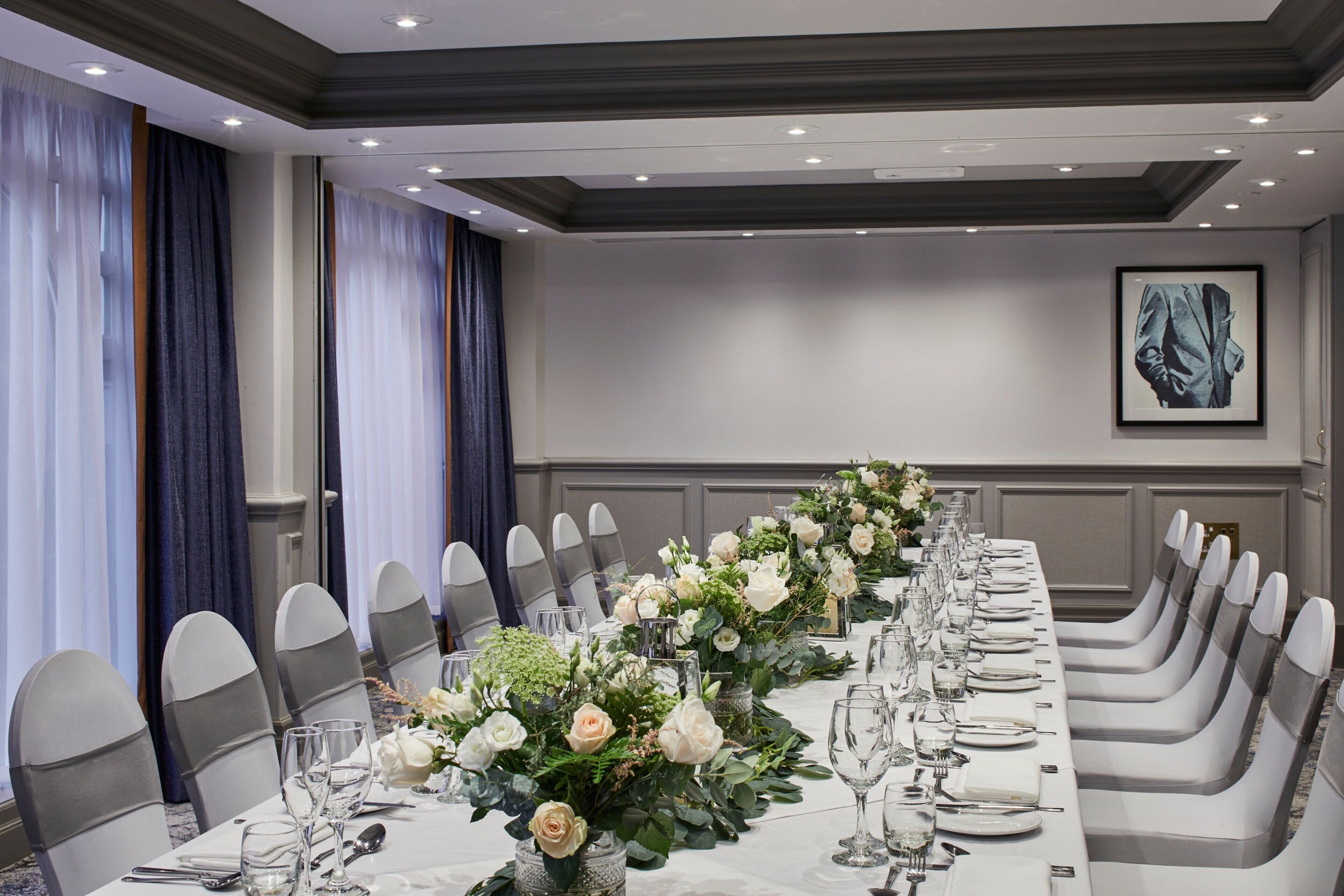 Une longue table à manger, dressée pour un événement formel, avec des chaises, de la verrerie et des centres de table floraux.