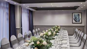 A long dining table set for a formal event with chairs, glassware, and floral centerpieces.