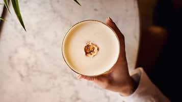 A hand holding a cup with a frothy beverage and a piece of food on top.