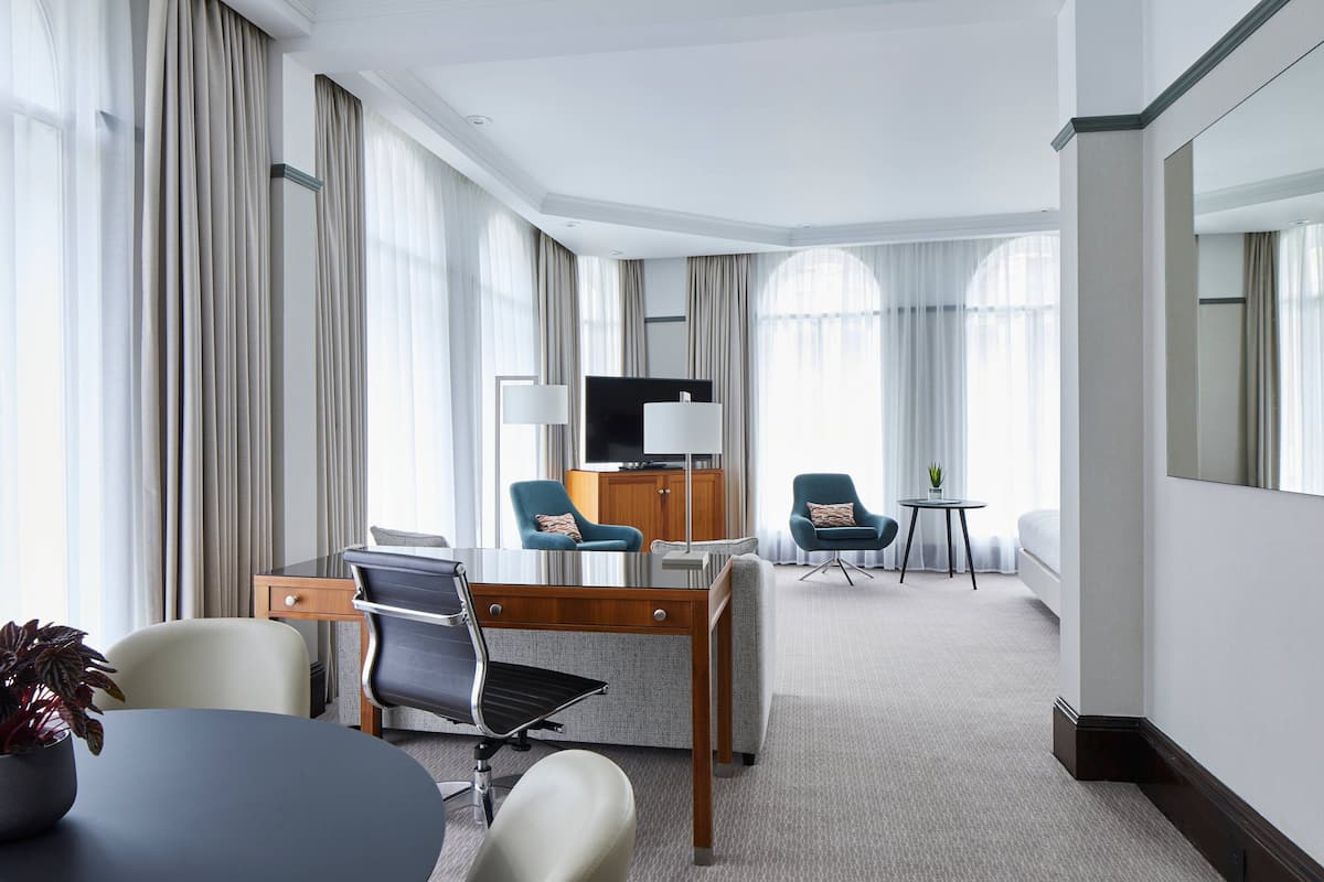A hotel room with a desk, two chairs, a TV, and a small table with a plant.