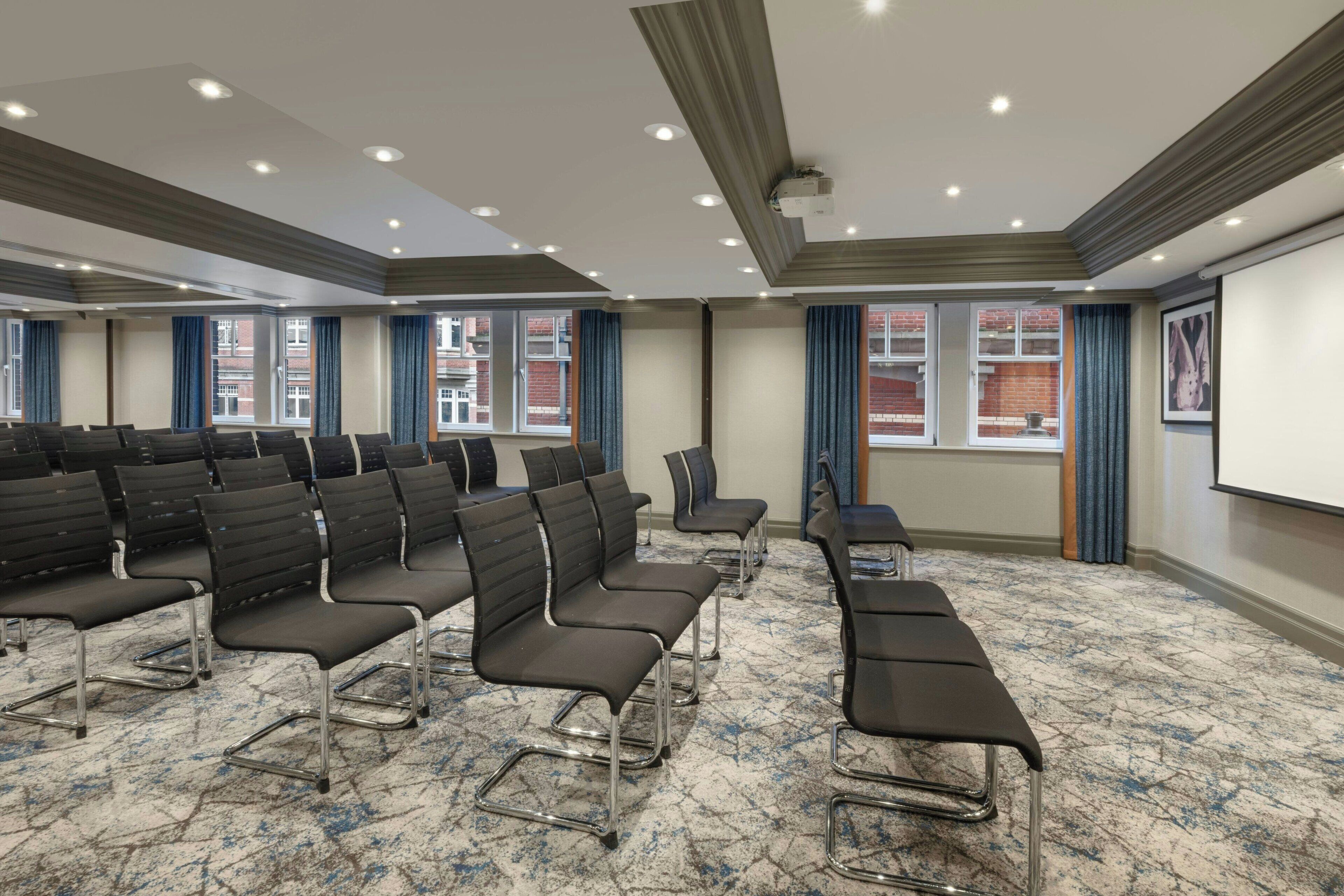 A conference room with rows of chairs, a projector screen, and large windows with curtains.
