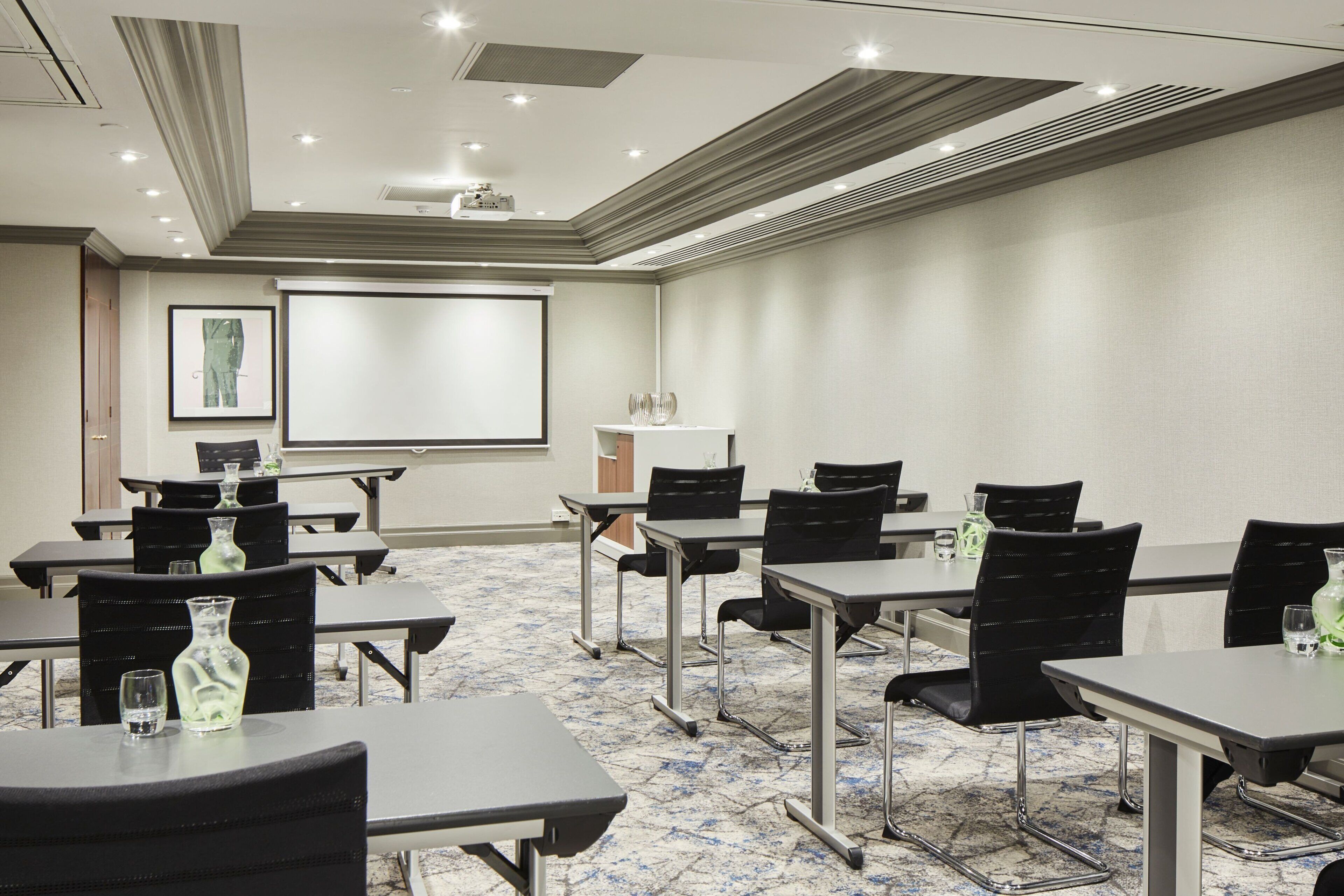 A conference room with tables, chairs, a projector screen, and a carpeted floor.
