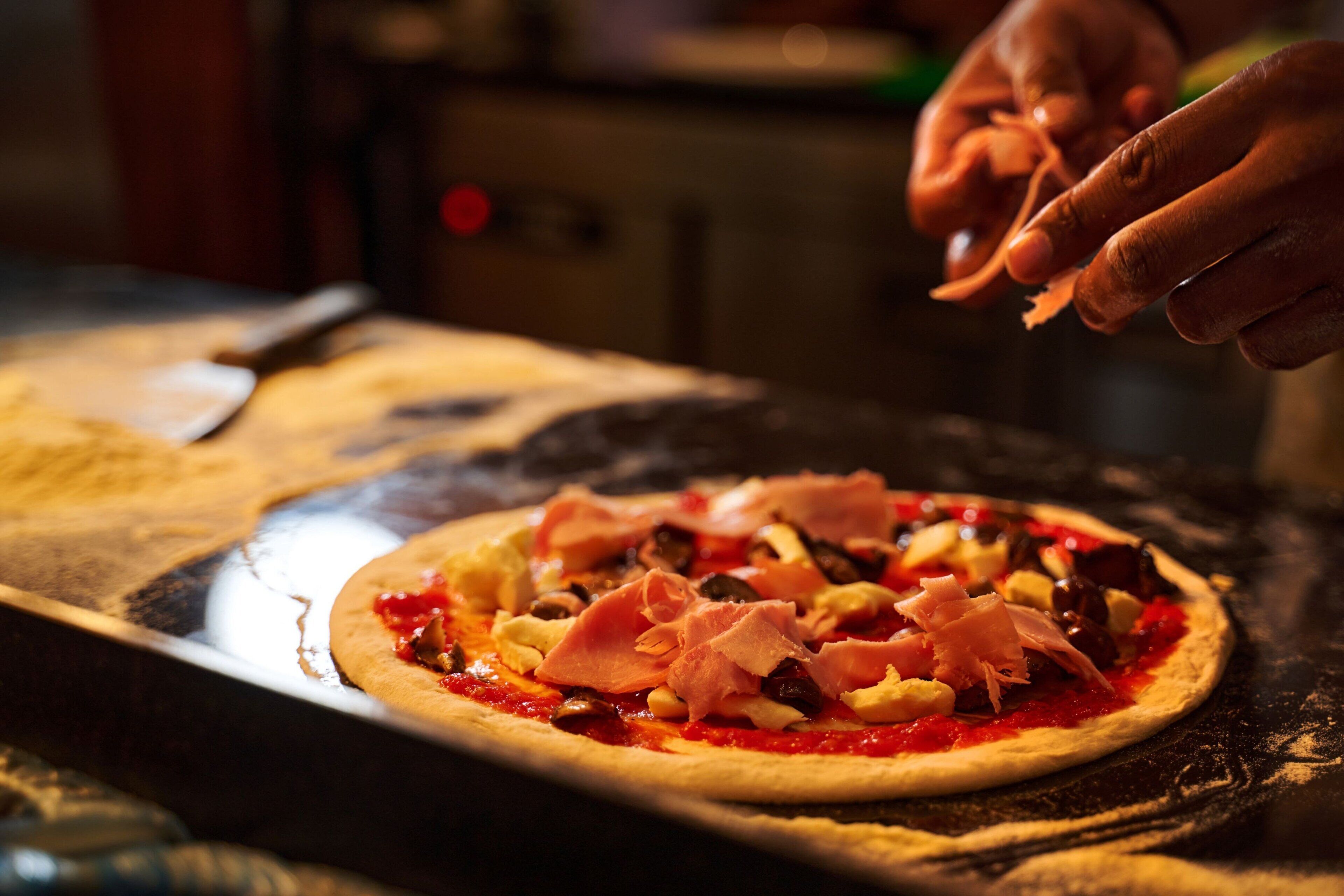 A pizza being prepared with toppings on a wooden surface.