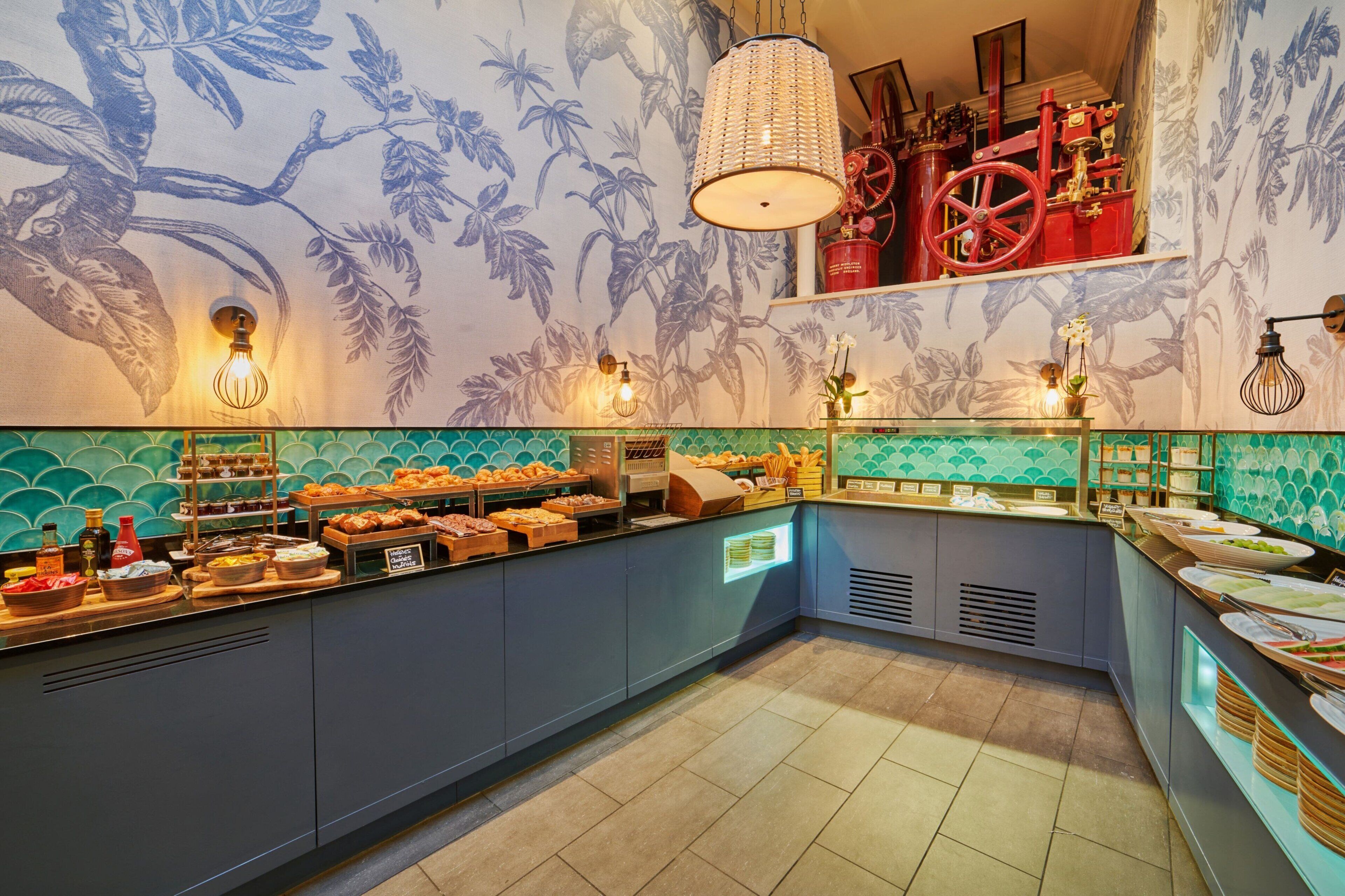 A buffet area with a variety of food items, a tropical-themed wall, and a vintage red machine.